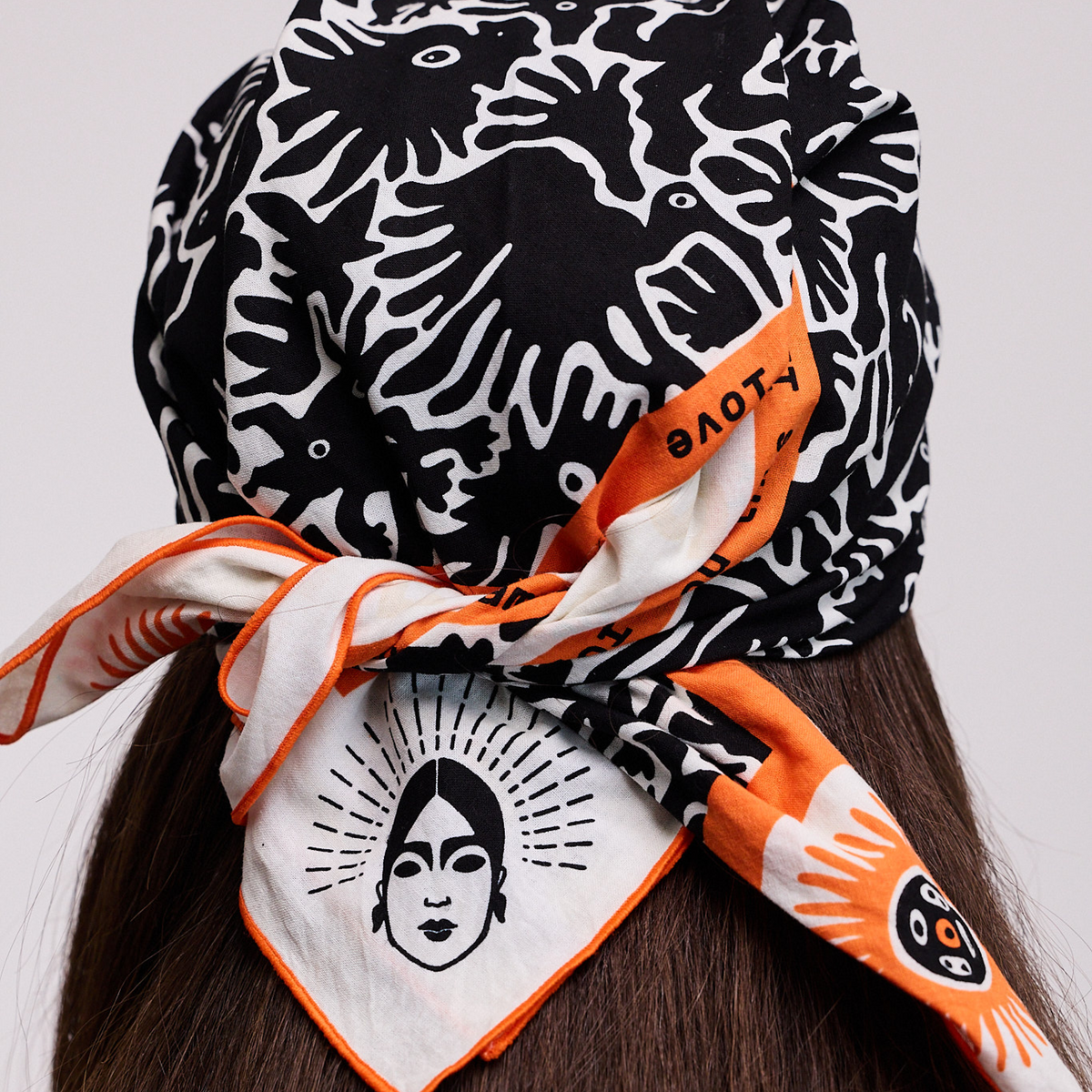 Back view of a Viva Maia black and white bandana with orange trim and face logo, tied at the nape of the neck.