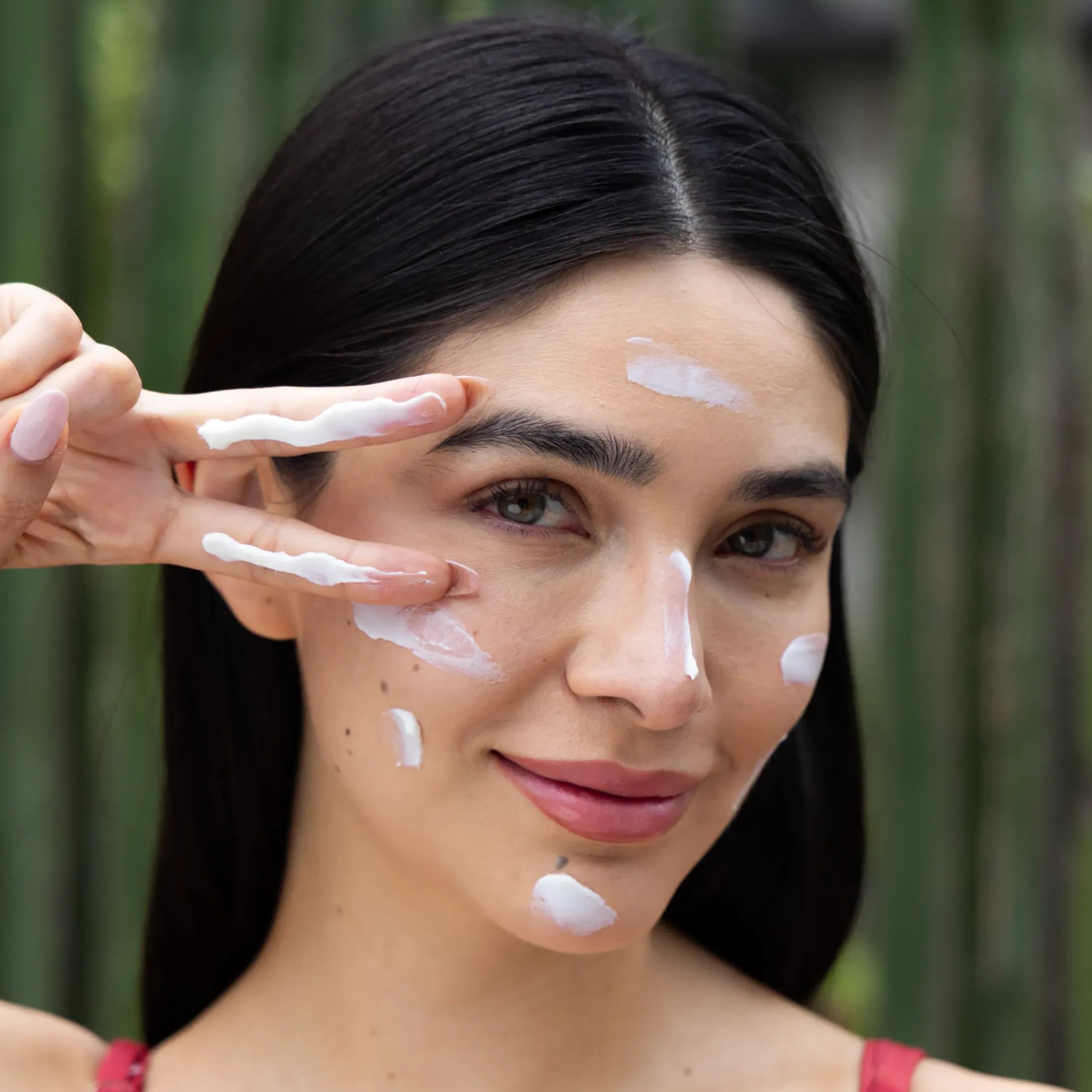 Frau trägt Viva Maia Shielding Sunscreen SPF 45+ mit den Fingern im Gesicht auf, vor grünem Bambushintergrund.