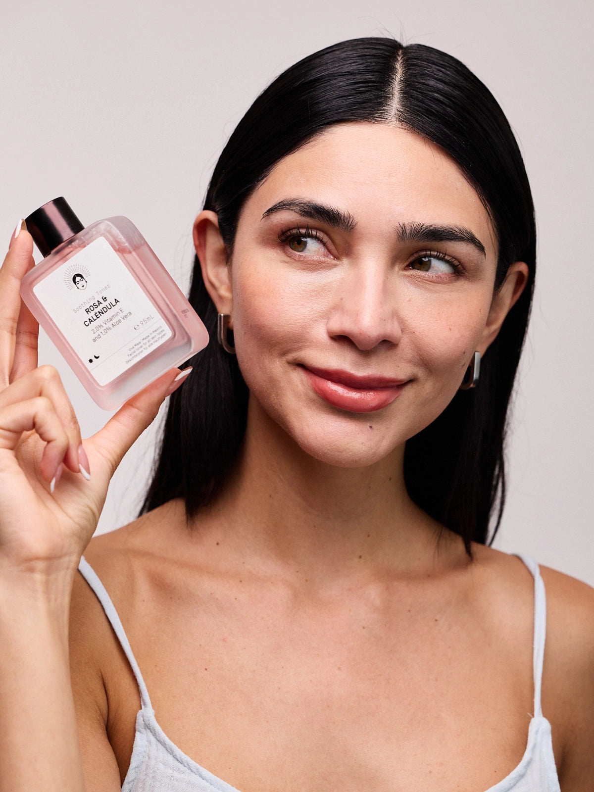 Viva Maia Rosa & Calendula Soothing Toner 95mL held beside a smiling woman's face.