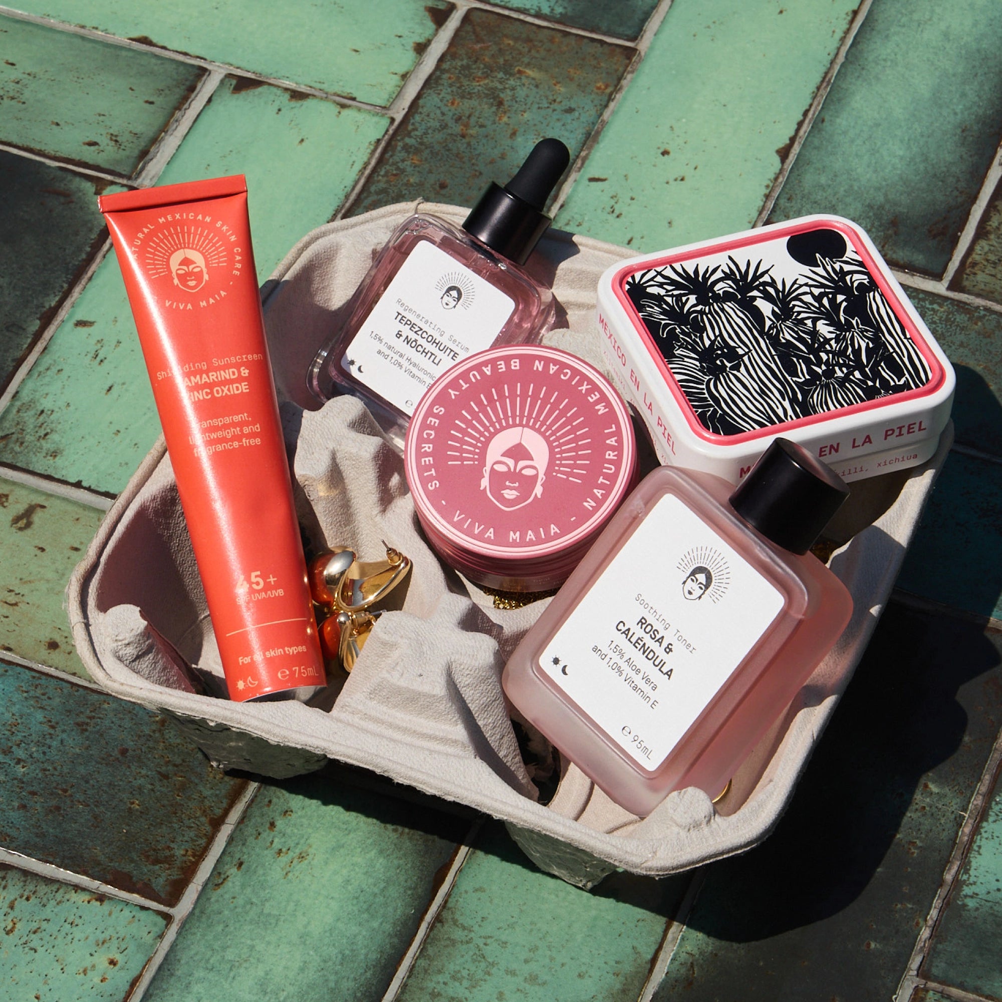 Viva Maia Set mit Shielding Sunscreen, Regenerating Serum und Soothing Toner auf grünen Fliesen in der Sonne.