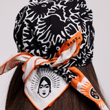 Back view of a Viva Maia black and white bandana with orange trim and face logo, tied at the nape of the neck.