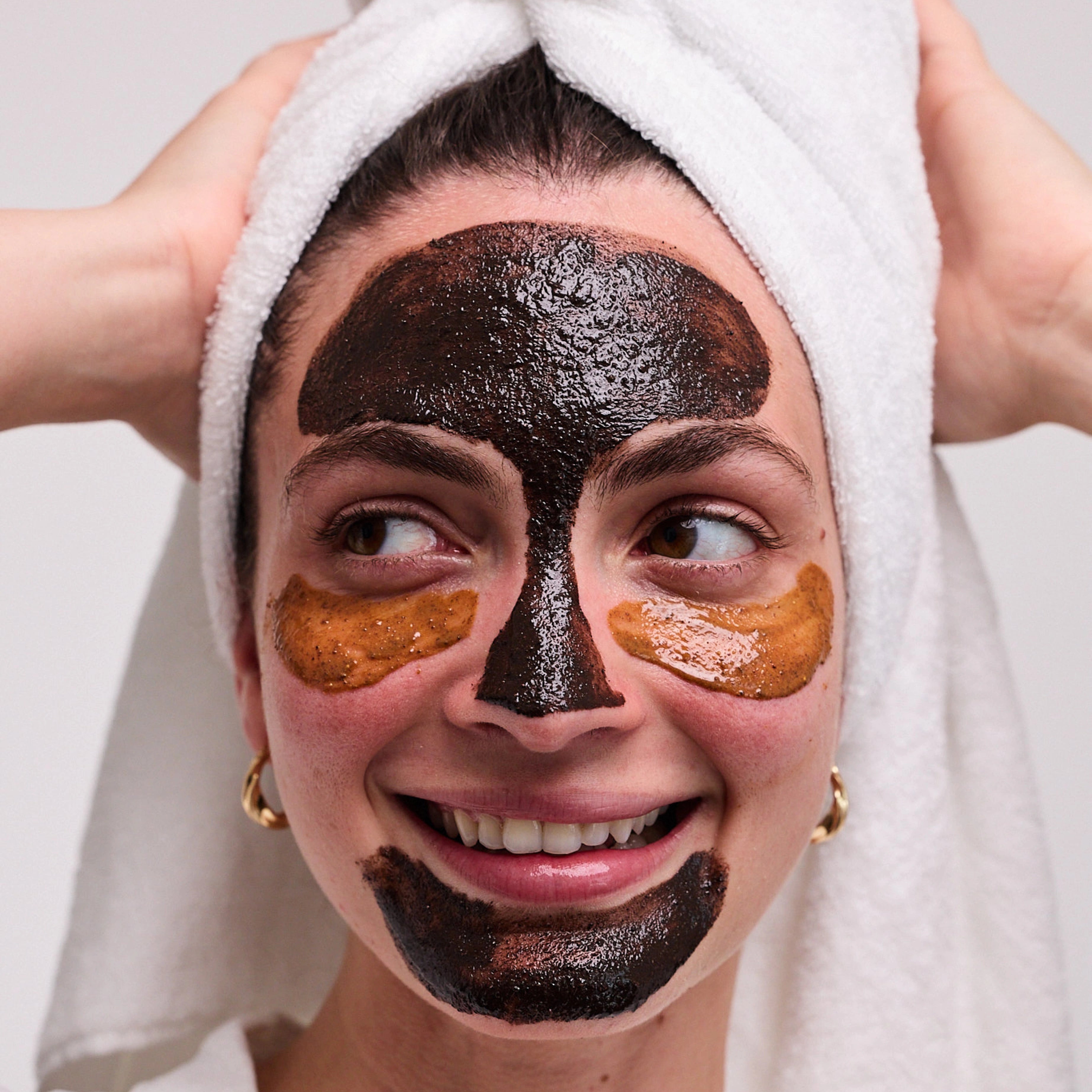 Smiling woman in a white towel turban with dark mask on forehead, nose and chin and golden eye patches