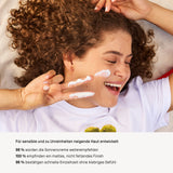 Lächelnde Frau im weißen Shirt trägt Viva Maia Shielding Sunscreen auf die Wange auf